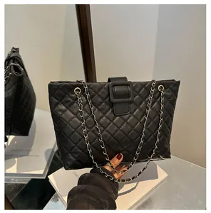 Detail of black quilted tote bag with chain strap and square buckle on smooth surface