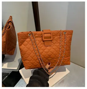 Detail of a quilted tote bag in brown orange with chain strap and square buckle