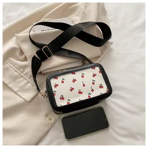 Mini bolso bandolera con estampado de cerezas y correa ancha junto a un móvil para tamaño