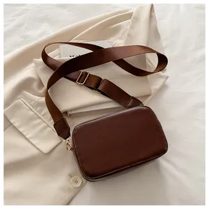 Detalle de bolso bandolera marrón con correa de nailon ancha sobre fondo de blazer beige