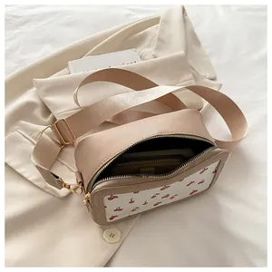 Detalle del bolso bandolera beige con estampado de cerezas y correa de tela ancha