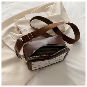 Vista detallada del bolso bandolera marrón con panel estampado de cerezas y correa ancha