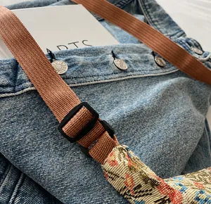Detail of adjustable buckle on denim shoulder bag with floral embroidery accents