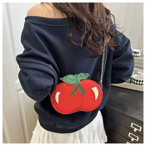 Detalle del bolso bandolera en forma de cereza roja con hojas verdes y cadena dorada