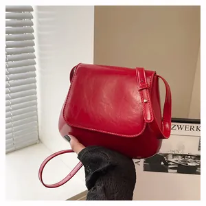 Detail of red glossy leather chestnut saddle bag showing hand-held size and metallic clasp