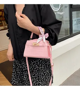 Detail of pink croc-embossed handbag featuring a gold twist lock and floral silk scarf handle