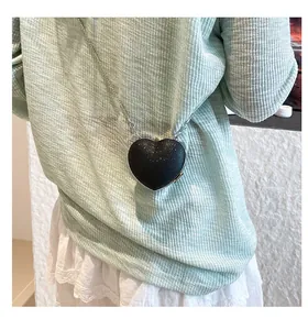 Close-up of black heart-shaped crossbody bag with silver chain on mint green top