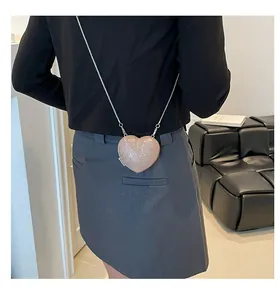 Rose gold sequin heart shaped clutch bag with silver chain strap worn by a model