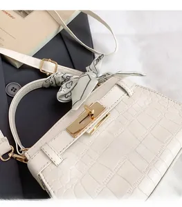 Detail of white crocodile-embossed handbag with gold clasp and decorative heart silk scarf