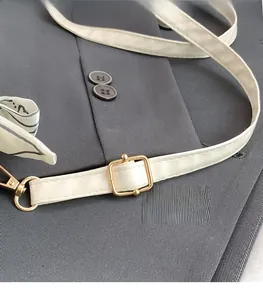 Detail of cream leather shoulder strap with gold buckle and silk scarf on grey blazer