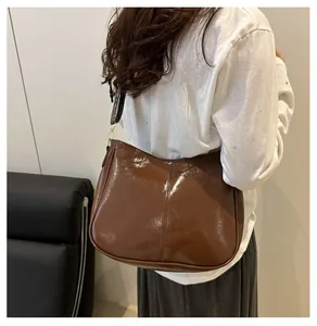 Detail of a brown glossy leather shoulder bag with a vintage pattern wide strap on model