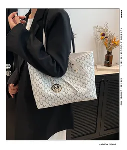 Detail of white tote bag with gray M pattern, long handles and metal M pendant