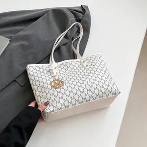 Detail of white tote bag with gray M-letter print and golden M-shaped pendant charm
