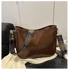 Detail of a brown glossy half-moon saddle bag with a bohemian geometric jacquard strap