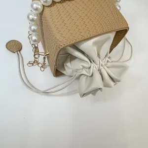 Detailed view of woven bucket bag featuring pearl handle and beige drawstring pouch