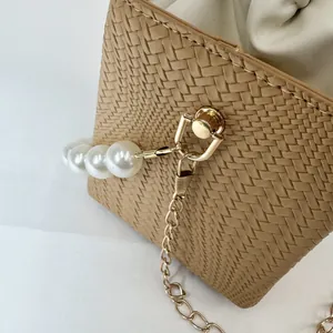 Detail of khaki woven bucket bag featuring large pearls and gold chain strap