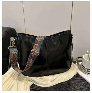 Detail of black glossy shoulder bag featuring a retro jacquard woven wide strap with patterns