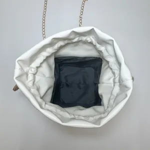 Internal view of a white drawstring bucket bag showing black lining and gold chain strap