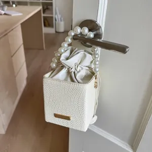 Detail of white woven bucket bag with pearl handle and drawstring lining on door handle