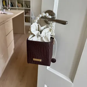 Detail of vintage bucket bag with pearl handle and woven leather texture hanging on a door