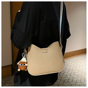 Close-up of beige crossbody bag with gold fashion plate and cute brown plush charm