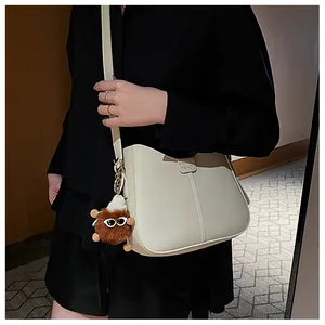 Detail of cream crossbody bag with wavy edge and cute brown plush charm accessory