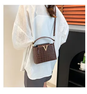 Detail of a brown crocodile embossed tote bag with gold V clasp on white shirt