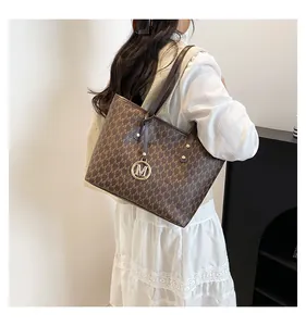 Detail of a brown monogram tote bag with a golden M logo charm on a white sleeve model