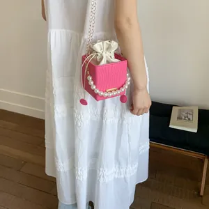 Pink drawstring bucket bag with pearl handle and wave texture worn by a model
