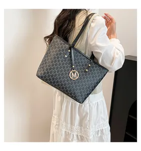 Detailed macro view of black faux leather tote bag with silver M pattern and metal charm