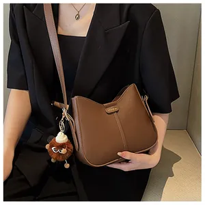 Brown faux leather crossbody bag detail with plush ball charm and fashion label tag