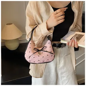 Sac hobo plissé rose avec imprimés nœuds et pendentif cœur porté par un mannequin