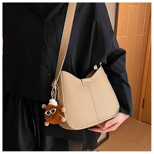 Detail of light brown crossbody bag featuring matte leather texture and plush charm