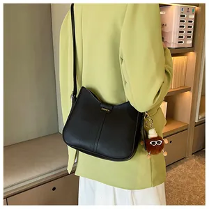 Detail of black faux leather half-moon bag featuring gold lettering and plush charm