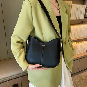 Minimalist black crossbody bag with gold FASHION text and wide strap on green blazer