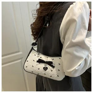Détail du sac à bandoulière blanc à nœuds avec pendentif cœur et tissu texturé élégant
