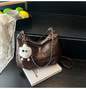 Detail of dark brown glossy leather hobo bag with chain strap and fluffy charm