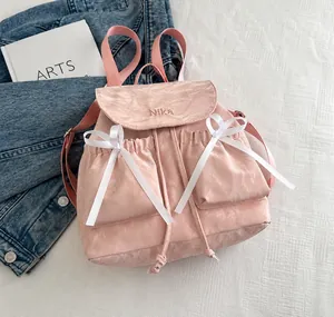 Detailed close-up of pink nylon backpack with embroidered logo and white satin bows