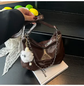 Detail of glossy brown patent leather tote with plush charm and chain strap