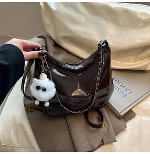 Detail of dark brown glossy tote bag with silver chain and white plush charm on side
