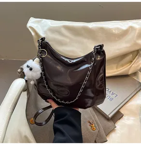 Detail of dark brown patent leather tote with metal chain and plush ball accessory