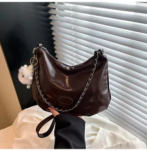 Detail of glossy brown patent leather hobo bag with silver chain and teddy charm
