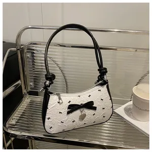 Détail du sac plissé blanc avec motifs de nœuds noirs et pendentif en forme de cœur