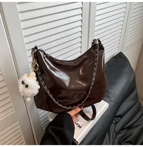 Detail of dark brown polished leather hobo bag with silver chain and plush charm pendant