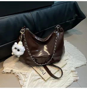 Close-up of chocolate brown patent leather tote with silver chain and plush charm