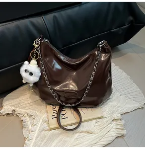 Close-up of a brown patent leather tote bag featuring a silver chain and a plush charm