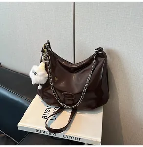 Detail of dark brown glossy patent leather shoulder bag with a silver chain and plush charm