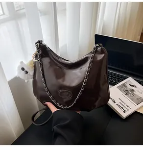 Detail of a shiny dark brown hobo bag with a silver chain strap and a white plush charm