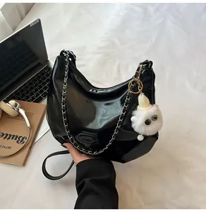 Detail of black patent leather tote bag with silver chain strap and plush monster charm