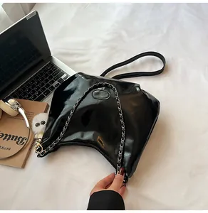 Detail of black patent leather hobo bag with metal chain strap and white plush charm